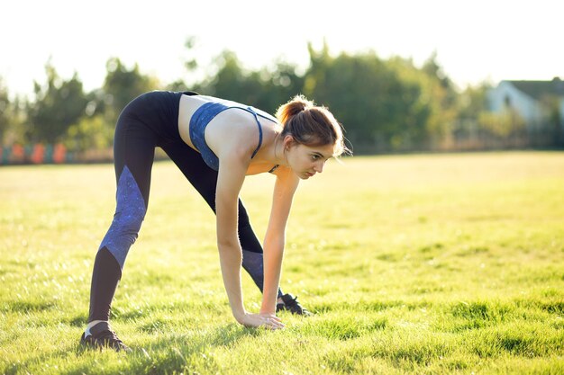 Giovane donna sportiva facendo esercizi di fitness sull'erba verde in una calda giornata estiva all'aperto.
