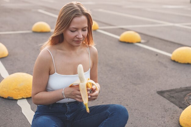 Giovane donna sportiva hipster che si prende una pausa dallo skate che corre mangiando banana