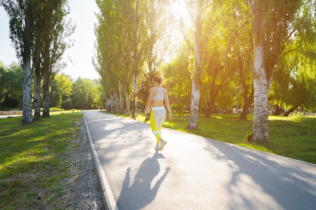 Giovane donna sportiva in abiti sportivi che corre nel parco di mattina