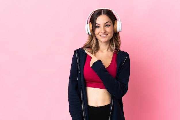 Giovane donna sportiva rumena isolata su sfondo rosa che punta al lato per presentare un prodotto