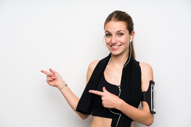 Giovane donna sportiva sopra il muro bianco isolato che punta il dito verso il lato