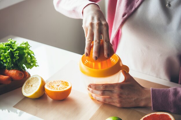 Giovane donna spremere il succo di arancia in cucina utilizzando uno spremiagrumi