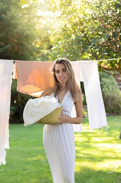 Giovane donna squisita in piedi davanti ai vestiti appesi che guarda alla macchina fotografica nel giardino