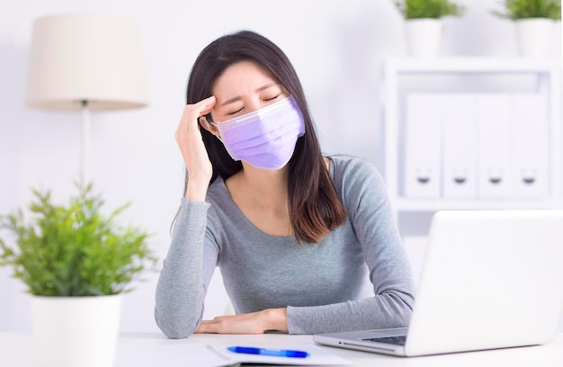 Giovane donna stressata che indossa una maschera medica e lavora in ufficio a casa