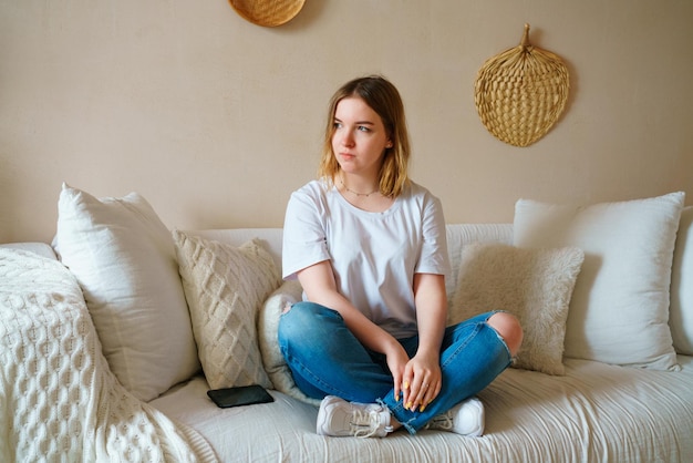 Giovane donna stressata seduta sul divano in abiti casual preoccupata per i problemi da sola a casa ha paura...