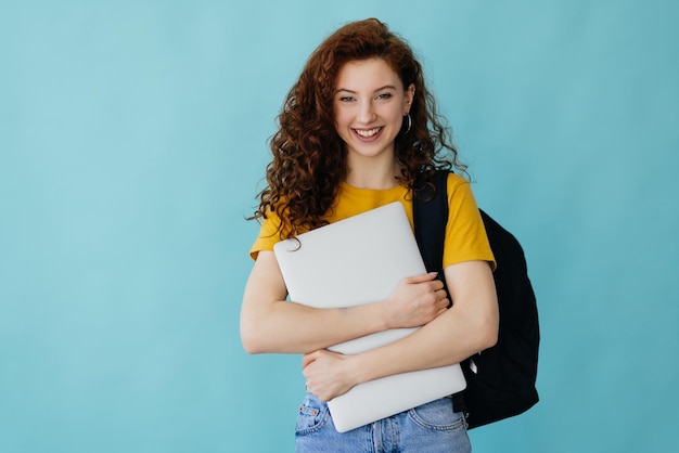 Giovane donna studente zaino tenere pc isolato su sfondo blu parete ritratto in studio Istruzione nel concetto di college universitario di scuola superiore