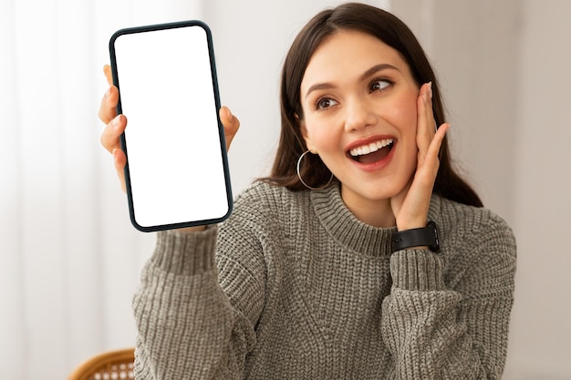 Giovane donna stupita alla ricerca di uno smartphone con schermo bianco