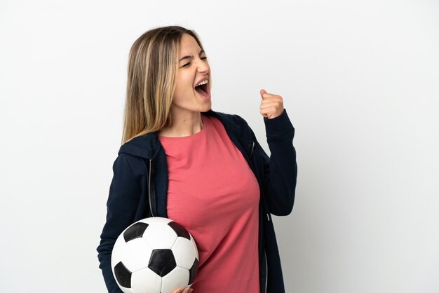 Giovane donna su sfondo bianco isolato con pallone da calcio che celebra una vittoria