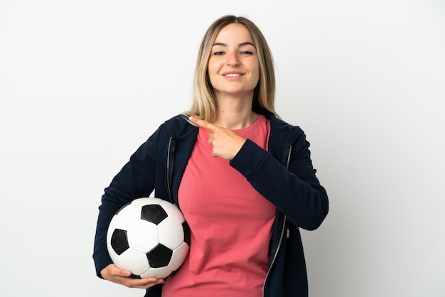 Giovane donna su sfondo bianco isolato con pallone da calcio e che punta al laterale