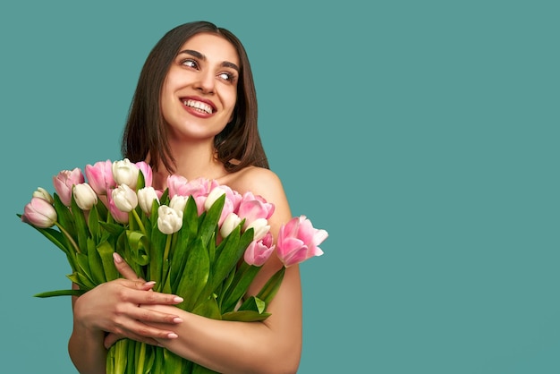 giovane donna su sfondo blu con in mano un bouquet di tulipani bianchi e rosa Concetto di primavera e di bellezza