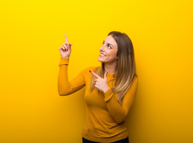 Giovane donna su sfondo giallo che punta con il dito indice e alzando lo sguardo