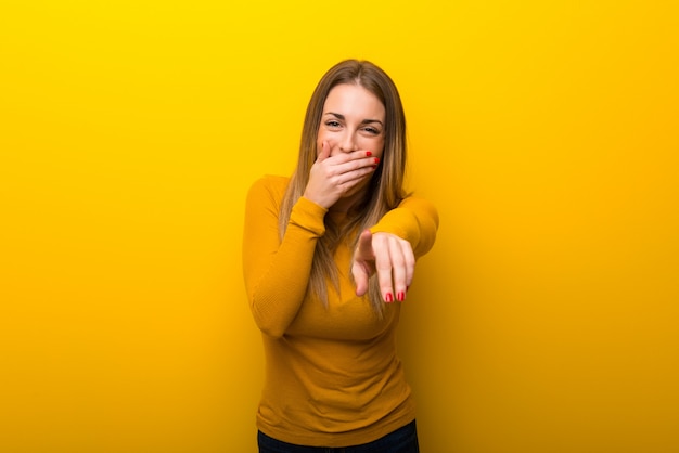 Giovane donna su sfondo giallo che puntava il dito contro qualcuno e ridendo