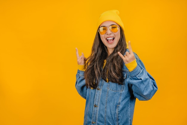 Giovane donna su sfondo giallo isolato che fa gesto rock