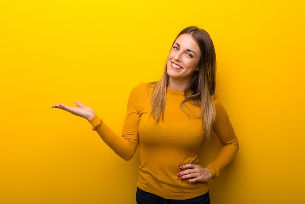 Giovane donna su sfondo giallo tenendo copyspace immaginario sul palmo per inserire un annuncio