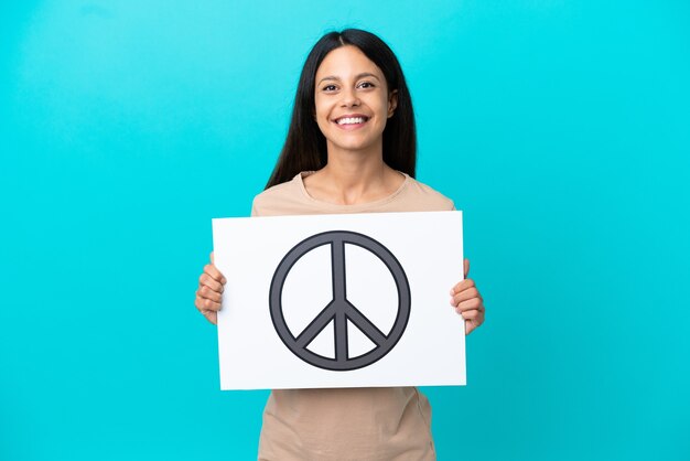 Giovane donna su sfondo isolato che tiene un cartello con il simbolo della pace con espressione felice