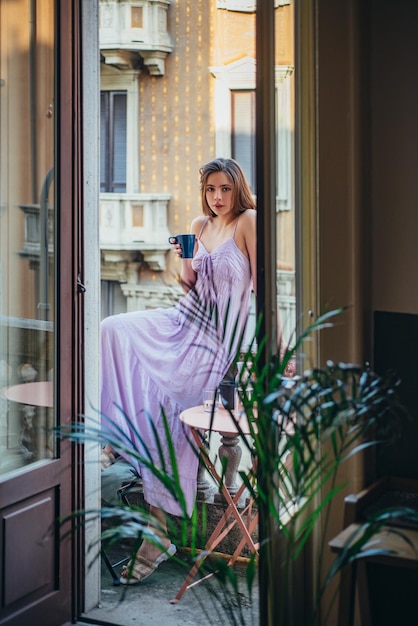 Giovane donna sul balcone con in mano una tazza di caffè o tè al mattino Bella donna che respira aria fresca sul balcone della villa al mattino Bella ragazza che si gode la freschezza