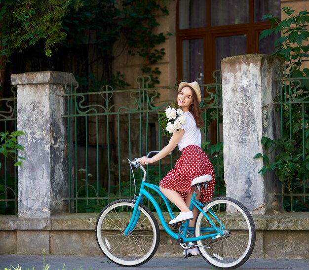 giovane donna sulla bici retrò blu con peonie