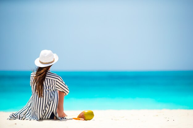 Giovane donna sulla spiaggia bianca con cocco