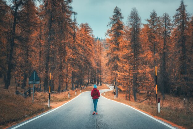 Giovane donna sulla strada nella foresta di autunno al tramonto