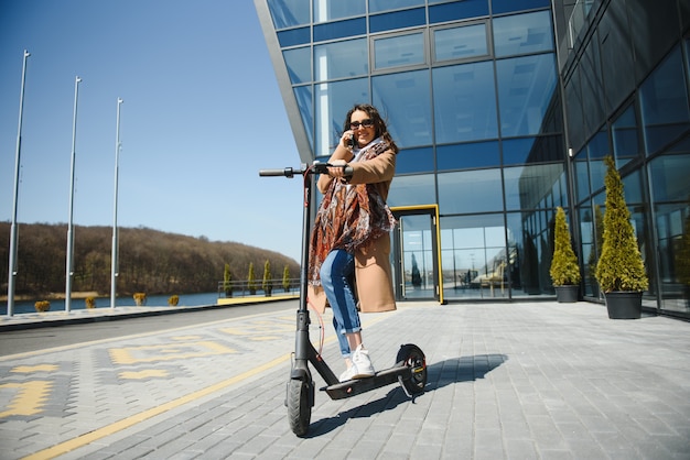 Giovane donna sullo scooter elettrico con edificio per uffici dietro, scooter