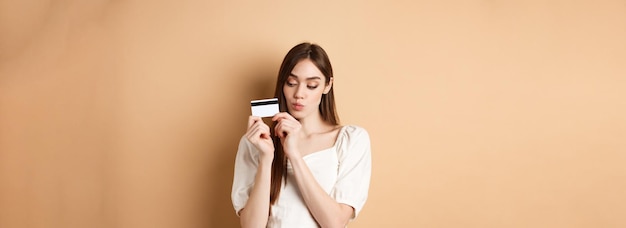 Giovane donna sveglia che osserva premurosa la carta di credito di plastica che pensa allo shopping che sta sul sedere beige