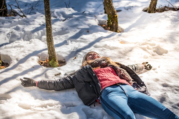 Giovane donna sveglia che si trova giocando e godendo della neve in inverno