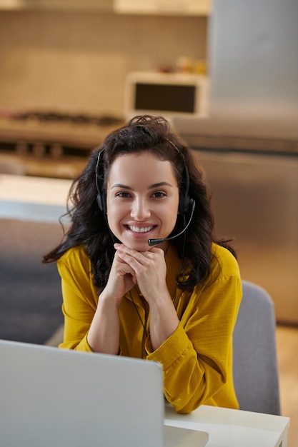 Giovane donna sveglia in una camicia di senape che si siede al computer portatile