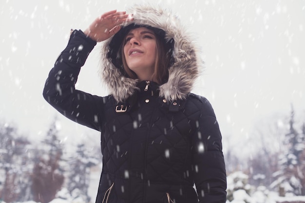 Giovane donna sveglia sotto i fiocchi di neve in inverno