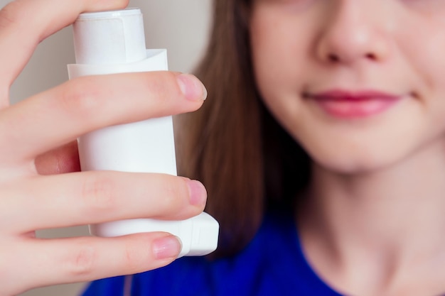Giovane donna teenager della ragazza che usa l'inalatore per l'asma a casa contro un fondo bianco della parete
