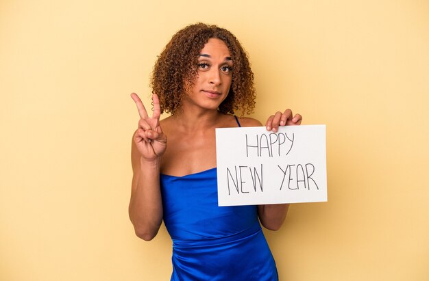 Giovane donna transessuale latina che celebra il nuovo anno isolato su sfondo giallo che mostra il numero due con le dita.