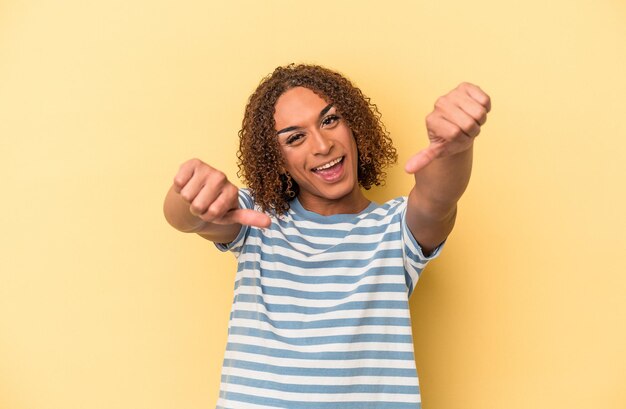 Giovane donna transessuale latina isolata su sfondo giallo alzando entrambi i pollici, sorridente e sicura di sé.