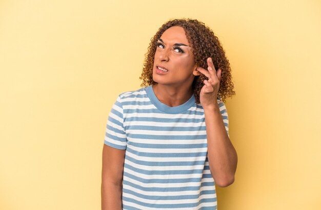 Giovane donna transessuale latina isolata su sfondo giallo che copre le orecchie con le dita, stressata e disperata da un ambiente rumoroso.