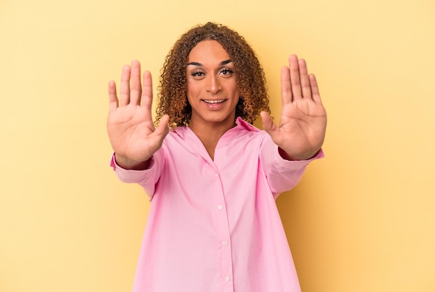 Giovane donna transessuale latina isolata su sfondo giallo che mostra il numero dieci con le mani.