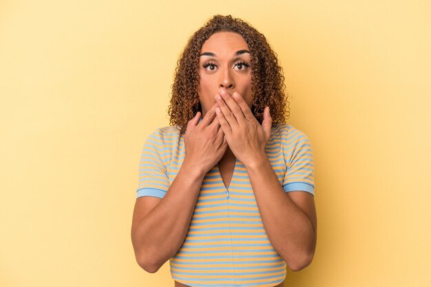 Giovane donna transessuale latina isolata su sfondo giallo scioccata, che copre la bocca con le mani, ansiosa di scoprire qualcosa di nuovo.
