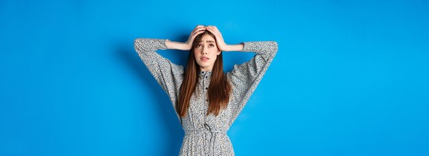 Giovane donna travagliata con i capelli lunghi che si tiene per mano sulla testa in preda al panico, alzando lo sguardo nervoso con problemi