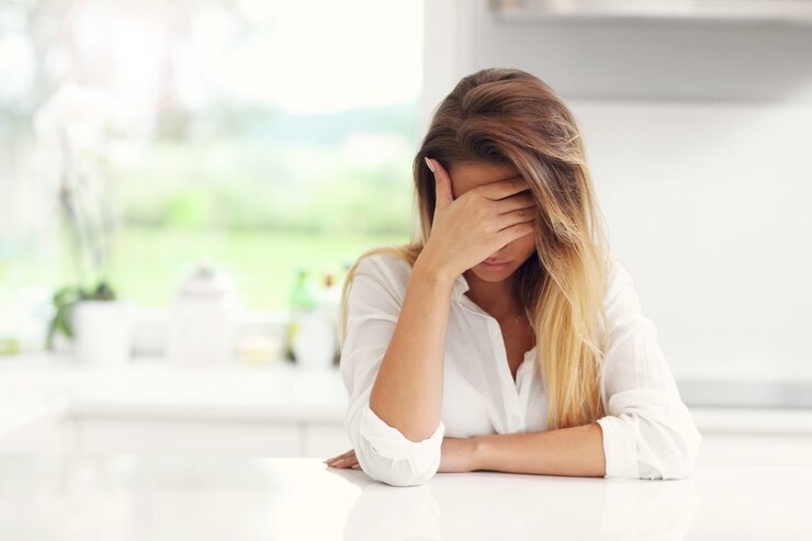 Giovane donna triste che soffre di mal di testa in cucina