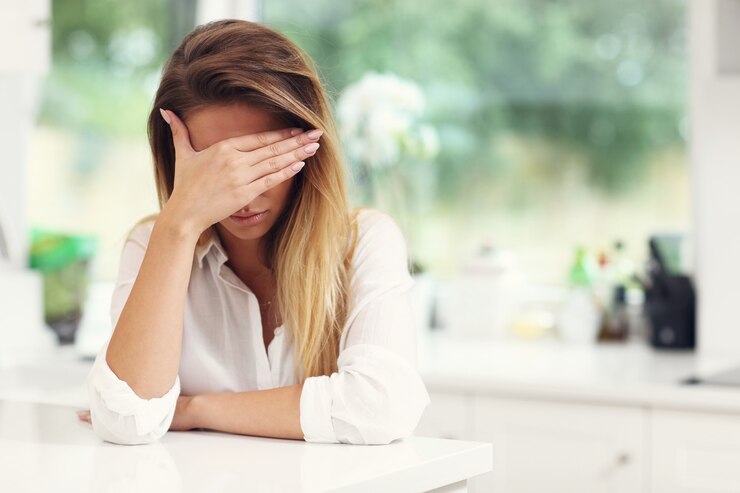 Giovane donna triste che soffre di mal di testa in cucina