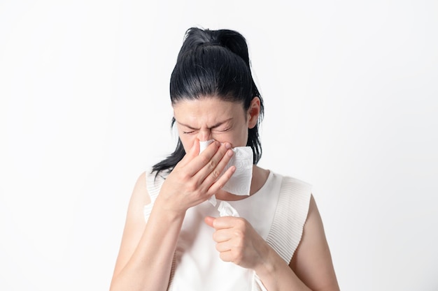 Giovane donna triste infelice che soffre di febbre e influenza che soffia il naso in un tovagliolo isolato su bianco