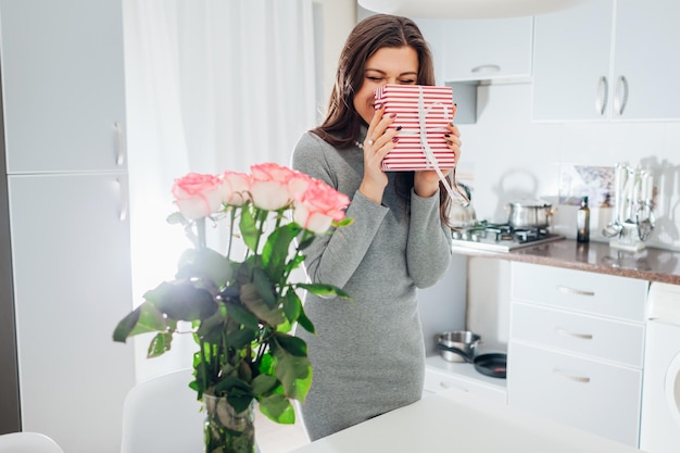 Giovane donna trovato confezione regalo e bouquet di rose in cucina ragazza sorridente felice che tiene presente