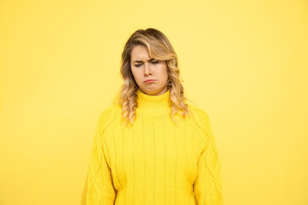 Giovane donna turbata su sfondo giallo, tristezza, donna triste turbata, preoccupata, prova a piangere. Colpo dello studio. Espressione facciale dello stress emotivo