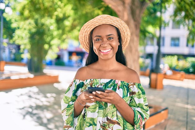 Giovane donna turistica afroamericana in vacanza sorridendo felice utilizzando lo smartphone in città