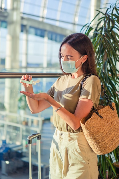 Giovane donna turistica in mascherina medica con bagagli in aeroporto internazionale