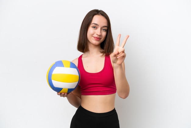 Giovane donna ucraina che gioca a pallavolo isolata su sfondo bianco sorridente e mostrando il segno della vittoria