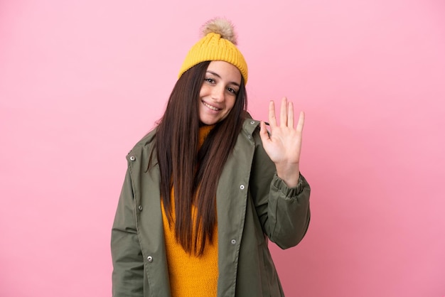 Giovane donna ucraina che indossa una giacca invernale isolata su sfondo rosa salutando con la mano con un'espressione felice