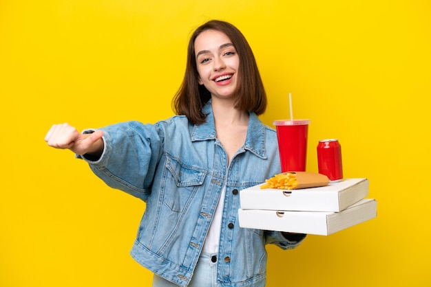 Giovane donna ucraina che tiene un fast food isolato su sfondo giallo dando un pollice in alto gesto