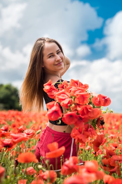 Giovane donna ucraina felice che tiene in mano un mazzo di fiori di papaveri che cammina e si gode la giornata di sole in campo