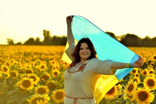 Giovane donna ucraina in abiti nazionali (vyshyvanka) con la bandiera ucraina in un campo di girasoli