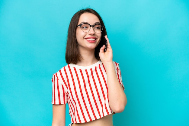 Giovane donna ucraina isolata su sfondo blu che mantiene una conversazione con il telefono cellulare