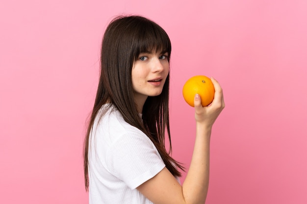 Giovane donna ucraina isolata su sfondo rosa in possesso di un arancio