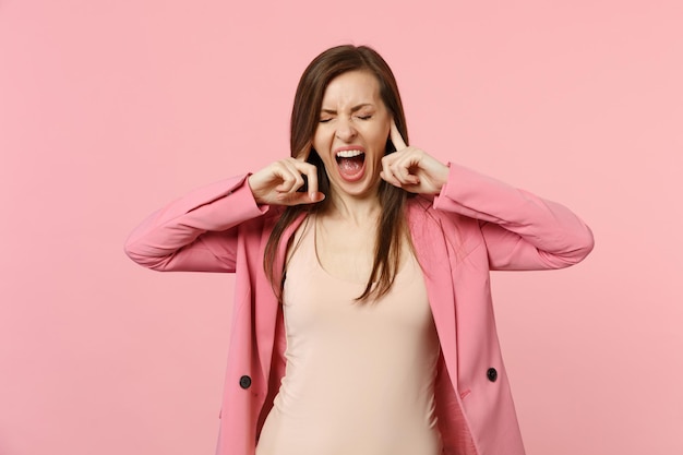 Giovane donna urlante pazza che indossa una giacca tenendo gli occhi chiusi, coprendo le orecchie con le dita isolate su sfondo rosa pastello in studio. Persone sincere emozioni, concetto di stile di vita. Mock up spazio di copia.